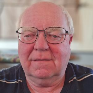 Colin Evans - a middle aged gentleman with balding grey hair and glasses. He is wearing a dark brown shirt with light coloured horizontal stripe.