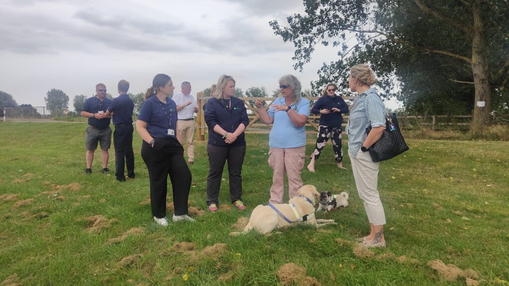 Tracey Clarke, founder Director of the Accessible Waterways Association (AWA), discussing accessibility of moorings with a group of personnel from the Environment Agency (EA). Her Guide Dog Loki is at her feet.