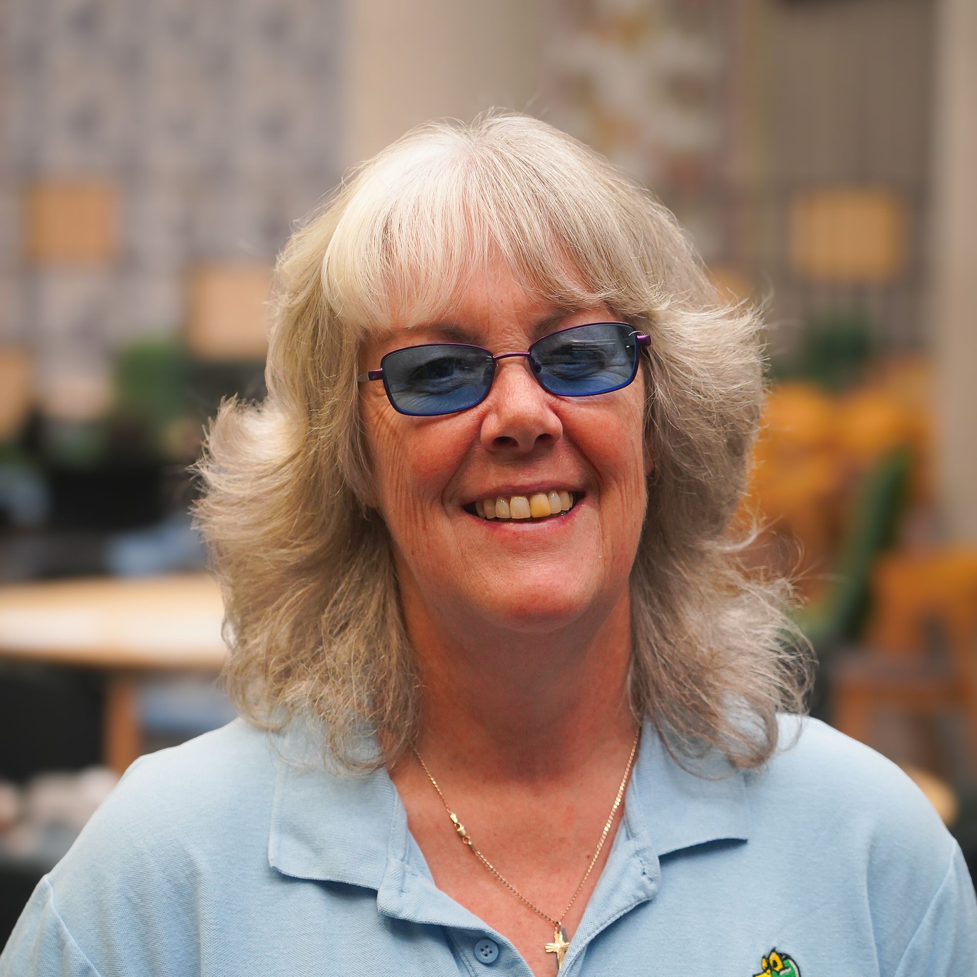 Tracey Clarke, Founder AWA. A middle-aged lady wearing dark glasses (as she is registered Severely Vision Impaired) with shoulder length light grey hair and a light blue top.