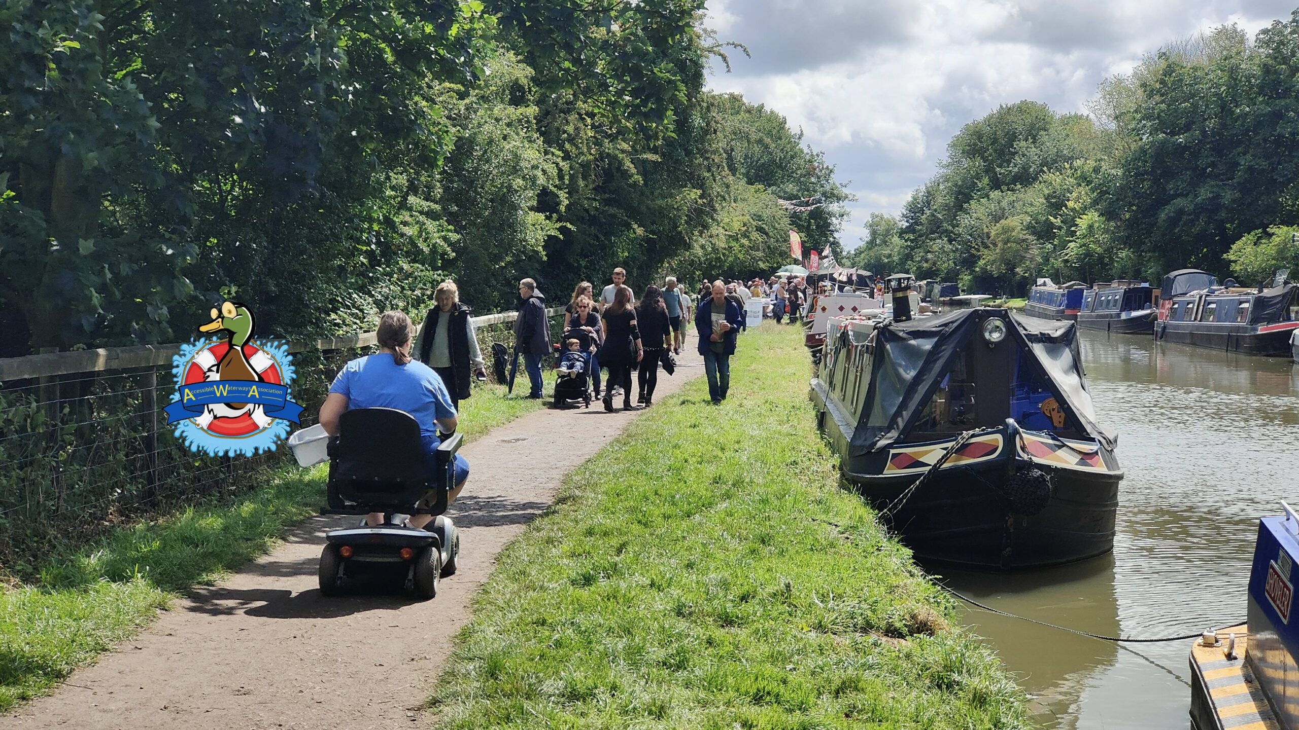 A wheelchair user heading away along a busy towpath, with moored boats alongside.